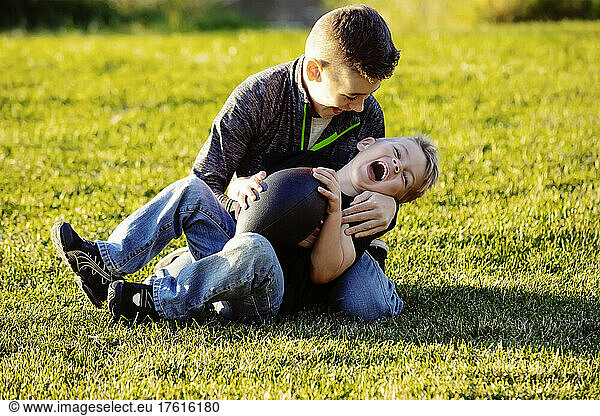 Two brothers roughhousing on the grass with a football; St. Albert  Alberta  Canada