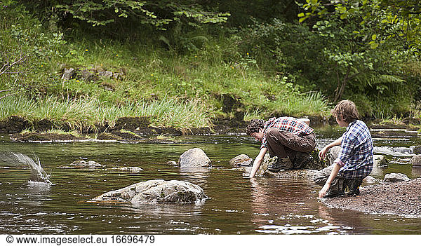 two brothers skipping stones at small river in the Brecon Beacons