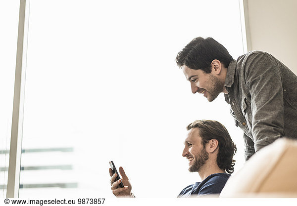 Two business men looking at a smart phone and smiling.