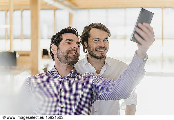 Two businessmen taking a selfie in wooden open-plan office