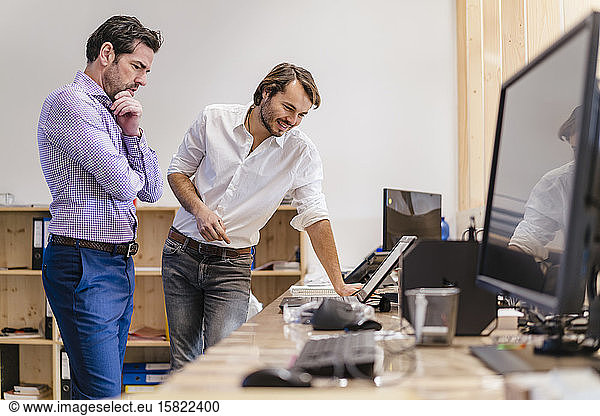 Two businessmen talking at desk in open-plan office