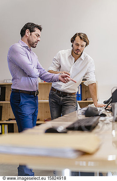 Two businessmen talking at desk in open-plan office
