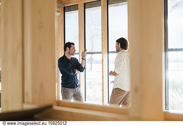 Two businessmen talking at the window in wooden open-plan office