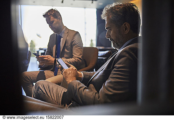 Two businessmen using smartphones in hotel lobby