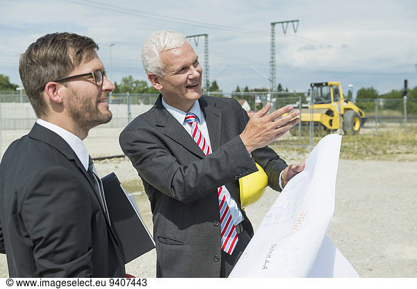 Two businessmen with construction plan on construction site