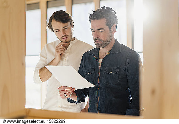 Two businessmen with document in wooden open-plan office