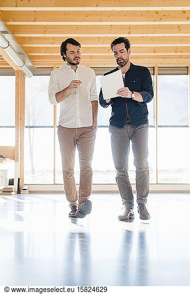 Two businessmen with documents talking in wooden open-plan office