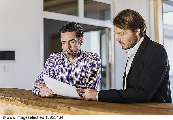 Two businessmen with documents talking in wooden open-plan office