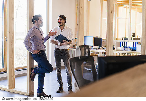 Two businessmen with folder talking in wooden open-plan office