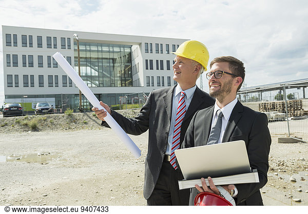 Two businessmen with hard hats on construction site