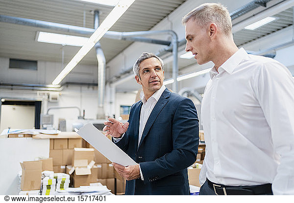 Two businessmen with paper talking in a factory