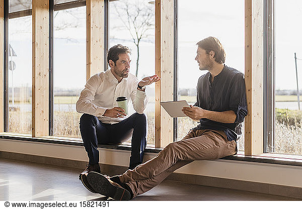 Two businessmen with tablet talking at the window in open-plan office