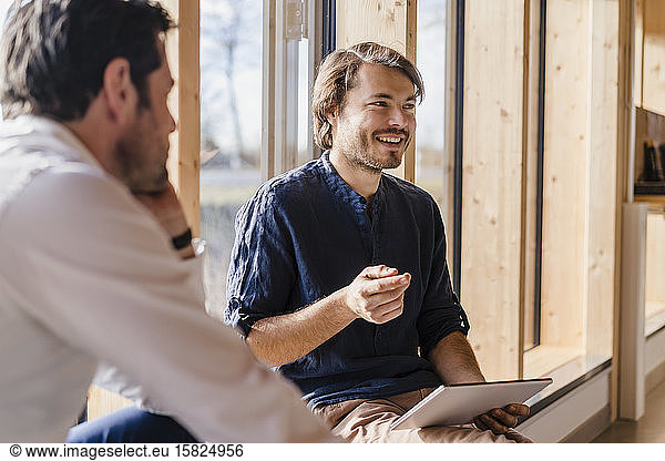 Two businessmen with tablet talking at the window in open-plan office