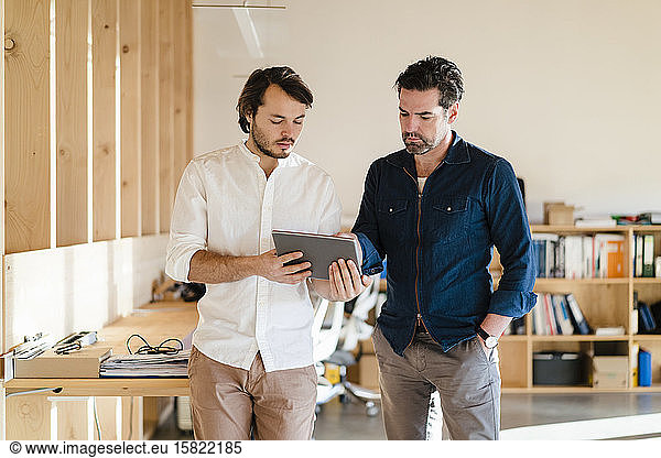 Two businessmen with tablet talking in wooden open-plan office