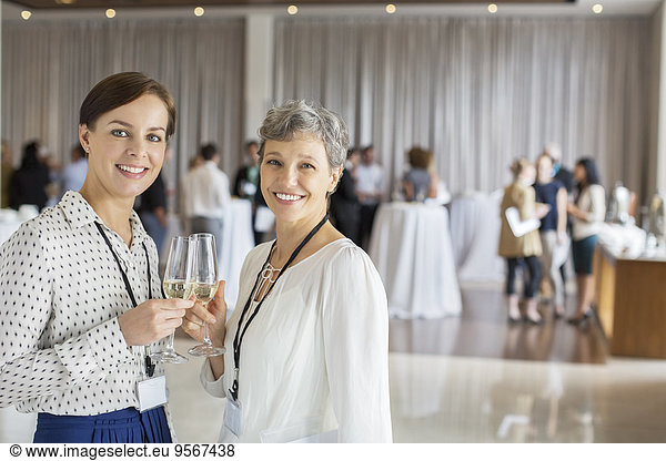 Two businesswomen standing with champagne flutes in hands  colleagues in background