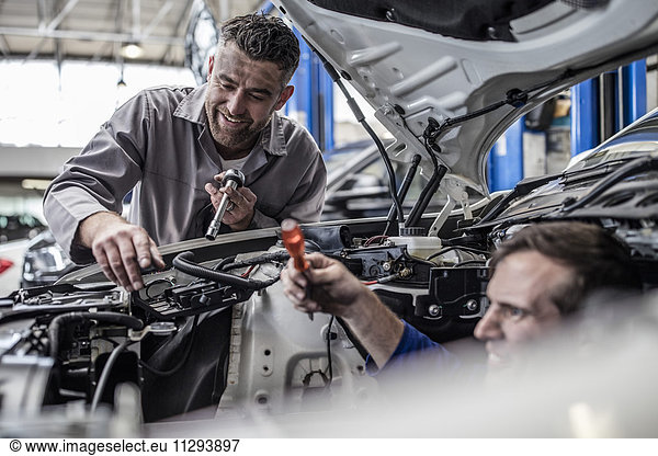 Two car mechanics in a workshop repairing car together