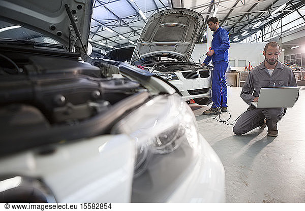 Two car mechanics with laptop in repair garage