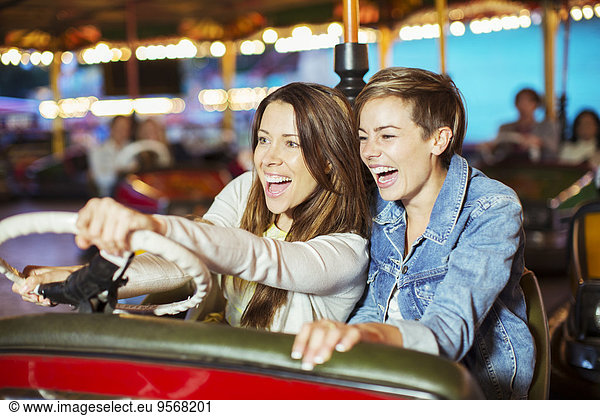 Two cheerful women on bumper car ride in amusement park