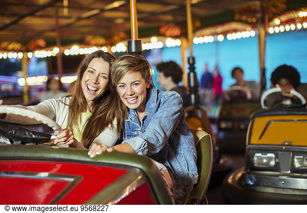 Two cheerful women on bumper car ride in amusement park