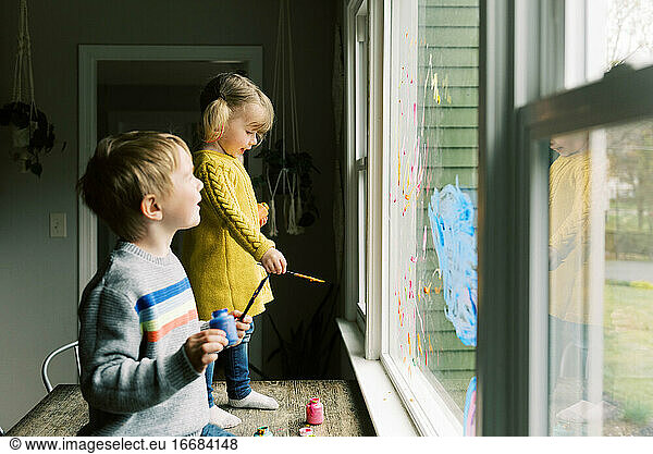 Two children coloring the kitchen window with finger parts together.