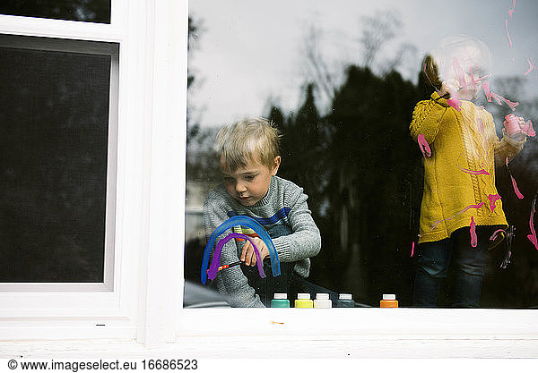 Two children coloring the kitchen window with finger parts together.