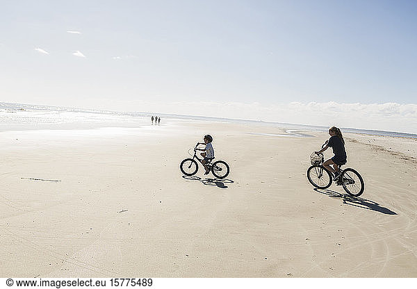Two children cycling on an open beach  a boy and girl.