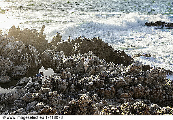 Two children exploring jagged rocks and rock pools by the ocean