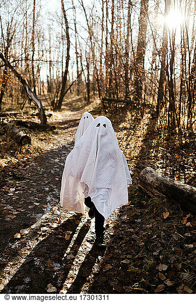 Two children in ghost costumes running in a park in the fall