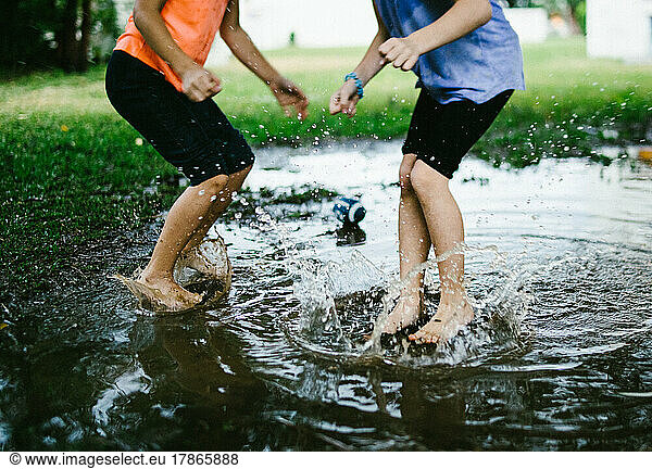 Two children jump into a rain puddle in green field