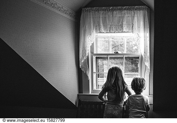 Two children look out a window.