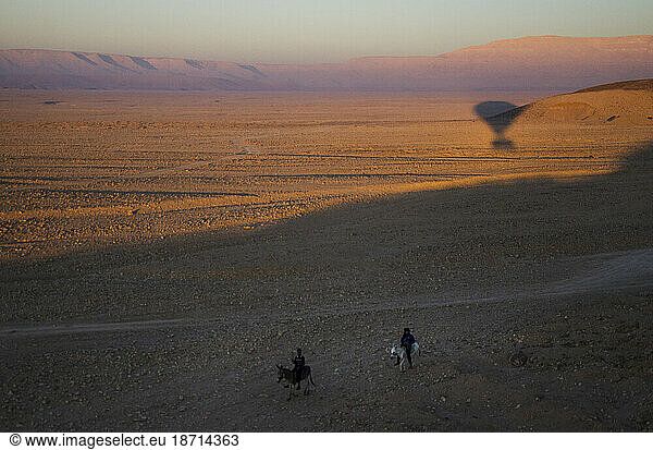 Two children on donkeys chase a hot air balloon in the Sahara