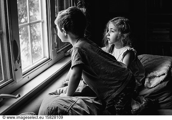 Two children perch on a couch and look out a window.