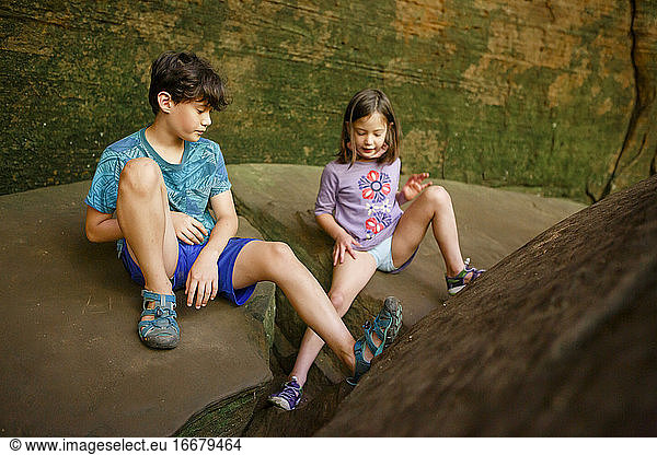 Two children play together on large boulder near a sandstone rock wall