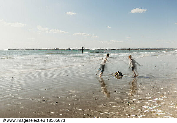 Two children running on beach against blue sky