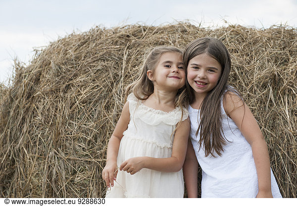 Two children seated together on a haystack talking.
