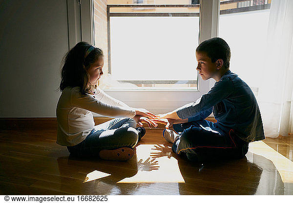 two children sitting on the floor playing with their hands in shadows