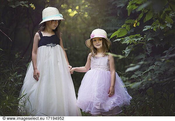 Two cute little girls in Easter dresses holding hands in the woods.