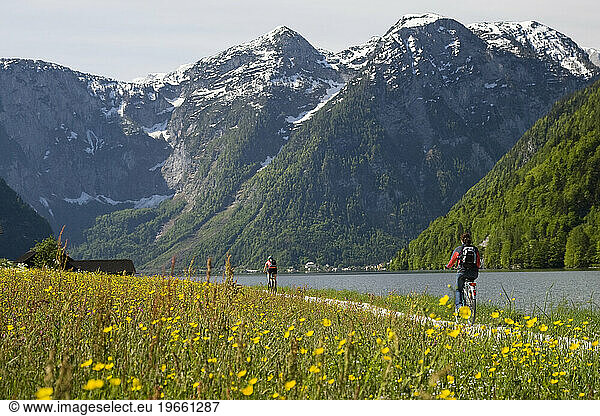 Two cyclists cycle along the shore of the Hallstatter See  Salzkammergut region  Austria.