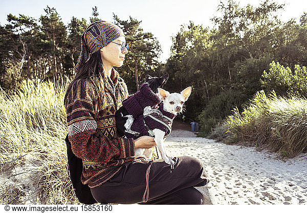 two dogs sit on womans lap in pretty sunlight on natural beach