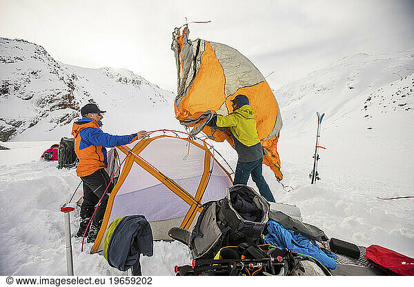 Two explorers work together to set up tent  clip on fly