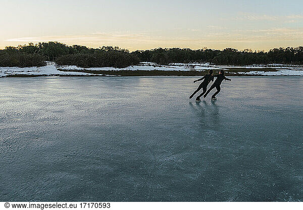 Two female figure skaters practicing together on frozen lake at dusk