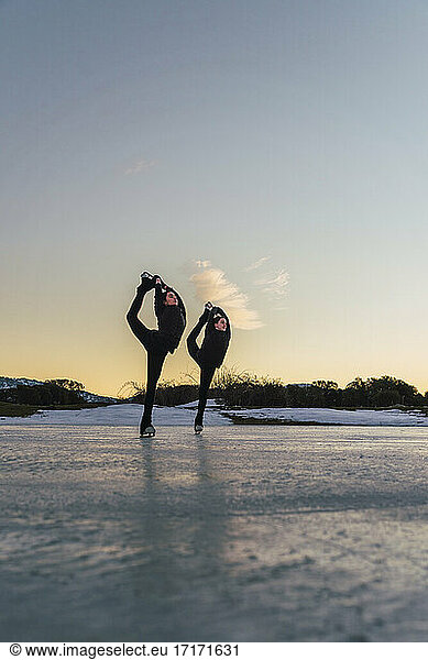 Two female figure skaters practicing together on frozen lake at dusk