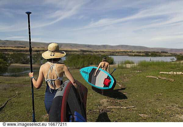 Two female friends carry their SUPs to the Columbia River in Oregon.