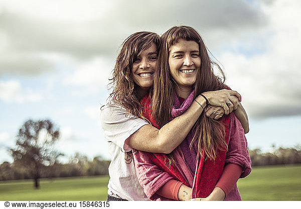 two female friends hug and laugh outdoors on green farm land