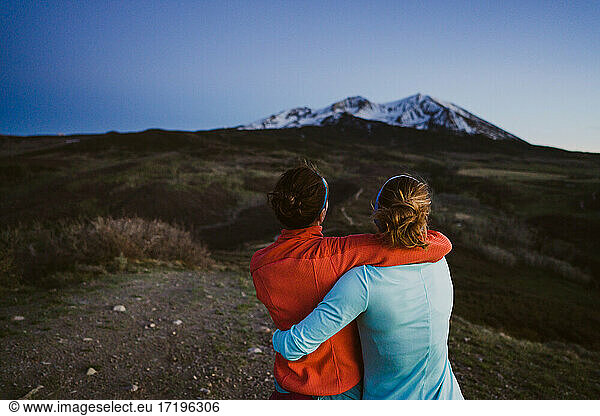 Two female friends hug and look out at mountain view at dusk