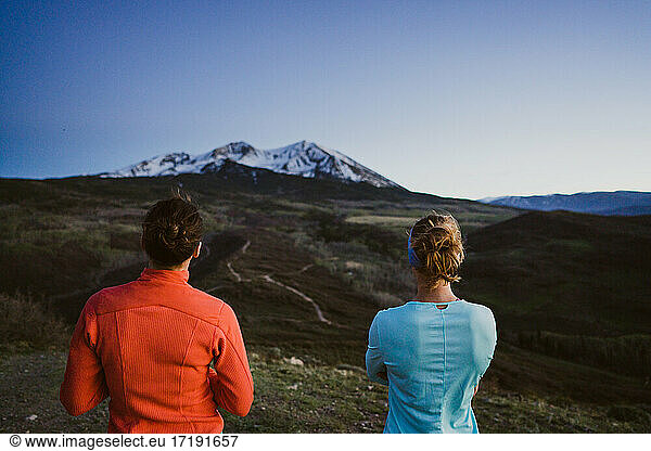 Two female friends look out at a mountain view together at dusk