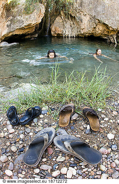 Two females enjoying a refreshing dip in a swim hole. Flip flops sitting on the edge of the hole. Crystal clear water.