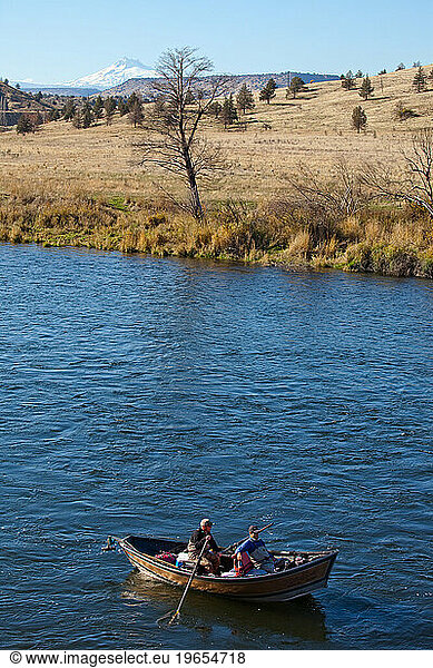 Two fisherman float down a river with mountains in the distance on a sunny day outside Bend  Oregon.