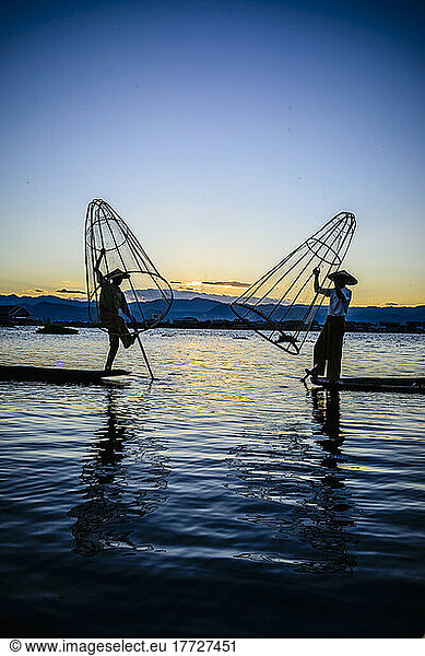 Two fishermen standing on their boats fishing on Lake Inle at dusk.