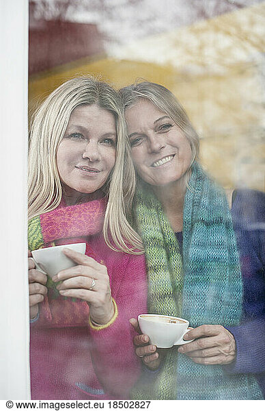 Two friends looking through window and drinking coffee in coffee shop  Bavaria  Germany